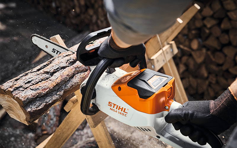 Man cutting with STIHL cordless chainsaw MSA 140 C-B fire wood in the garden close up