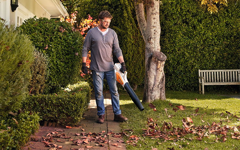 Man blows away autumn leaves on a side path in the garden with STIHL blower